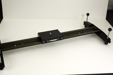 A black metal linear rail with a central sliding block and two vertical adjustment handles.