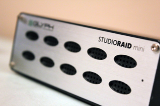 A silver StudioRAID mini device with several black circular ventilation holes on its top surface.