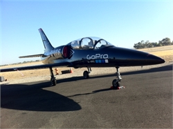 A black jet aircraft with GoPro branding parked on an asphalt runway under a clear blue sky.