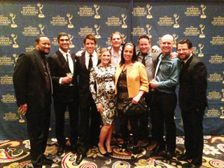 A group of eight people in formal attire posing together in front of a blue patterned backdrop.