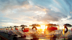 A row of clear laboratory containers sits outdoors against a bright sunset and cloudy sky.