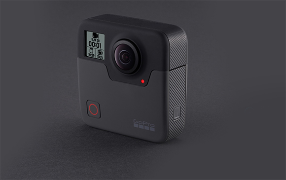 A black, square-shaped GoPro action camera with a small lens and a digital display screen.