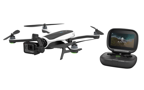 A white and black quadcopter drone with a mounted camera next to a handheld remote controller with a screen.