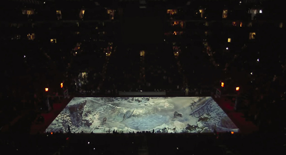 A bright rectangular screen showing a snowy landscape in a dark, crowded arena.
