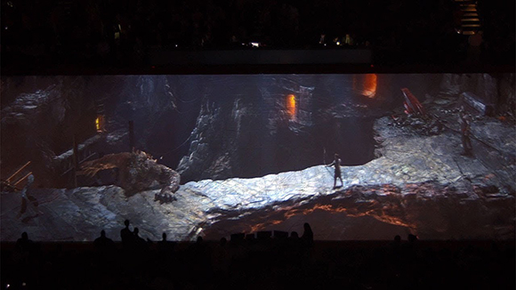 A stage set depicting a dark, rocky cavern with a large creature and a lone figure.