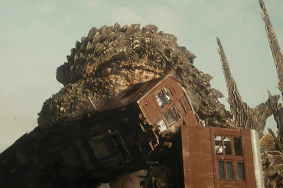 A massive, textured creature rises behind a derailed brown train car under a pale sky.