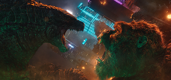A large green reptilian creature and a large brown ape face each other with mouths open in a city at night.