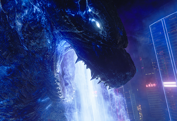 Close-up profile of a giant blue reptilian creature with its mouth open against a city backdrop.