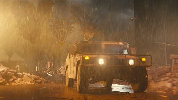 A military humvee drives through heavy rain toward a giant three-headed dragon in a dark, stormy setting.