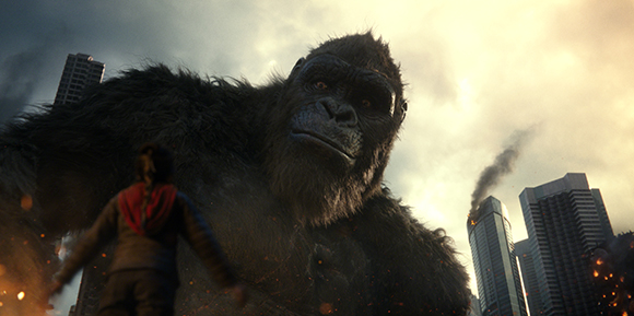 A massive dark gorilla towers over a person standing in a city with skyscrapers and smoke.
