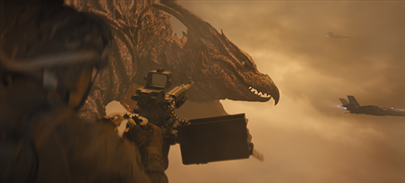 A massive dragon head looms in a cloudy sky near a person filming with a professional camera and two jets.