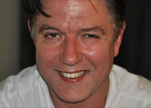 Close-up portrait of a man with dark hair smiling at the camera.