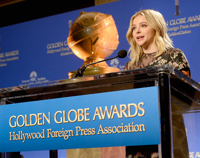 A blonde woman speaking behind a Golden Globe Awards podium with a large trophy in the background.