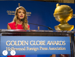 A woman in a red dress speaks into a microphone behind a Golden Globe Awards podium.