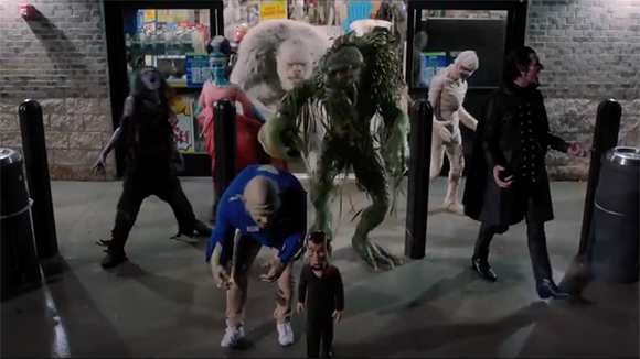 Various costumed monsters, including a swamp creature and a vampire, stand outside a storefront.