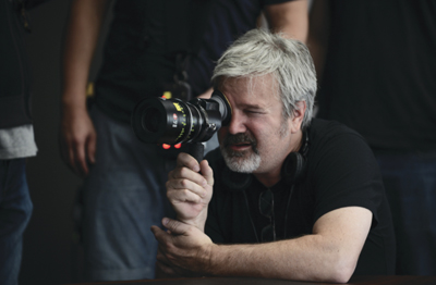 A man with gray hair and a beard looks through the viewfinder of a professional camera.