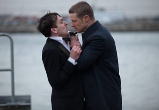 A man in a dark suit grabs another man by the collar near a body of water.