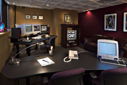 An office featuring several computer desks, a dark red wall with framed art, and a leather sofa.