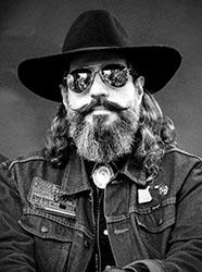 Black and white portrait of a man wearing a wide-brimmed hat, sunglasses, and a denim jacket.
