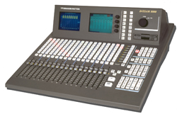 A dark gray digital audio mixing console with numerous sliders, buttons, and two small display screens.