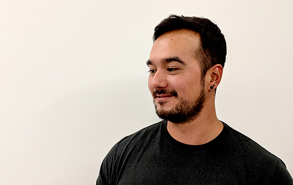 A man with dark hair and a beard smiling while looking to his left against a white background.