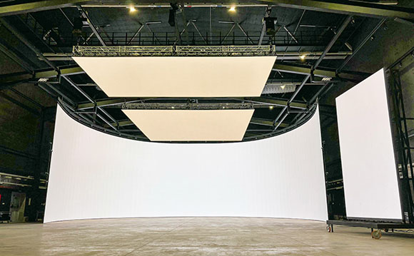 A wide shot of a large studio featuring curved white projection screens and overhead lighting rigs.
