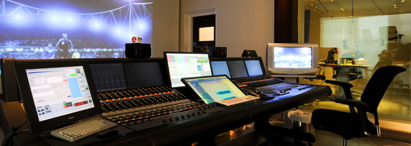 A large digital audio mixing console with multiple screens and monitors in a professional studio.
