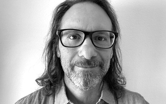 Black and white headshot of a man with long dark hair, glasses, and a salt-and-pepper beard.