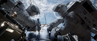 Two astronauts in white spacesuits working on a mechanical structure in space.