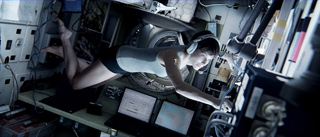 A person lies horizontally across a workspace filled with computer monitors and electronic hardware.