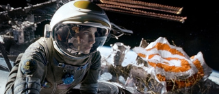 An astronaut in a white helmet floats in space near floating debris and a spacecraft structure.