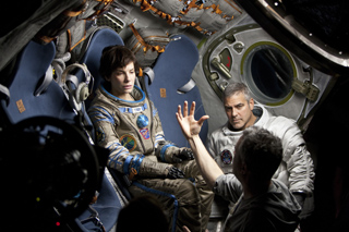 A young man in a spacesuit sits in a blue pilot seat inside a spacecraft cockpit.