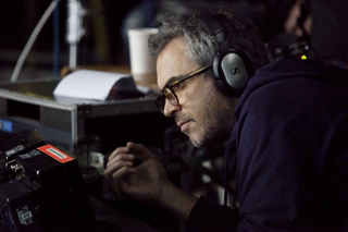 A man with glasses and headphones leans forward in a dark setting.