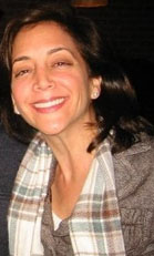 A smiling woman with dark hair wearing a white and grey plaid scarf.