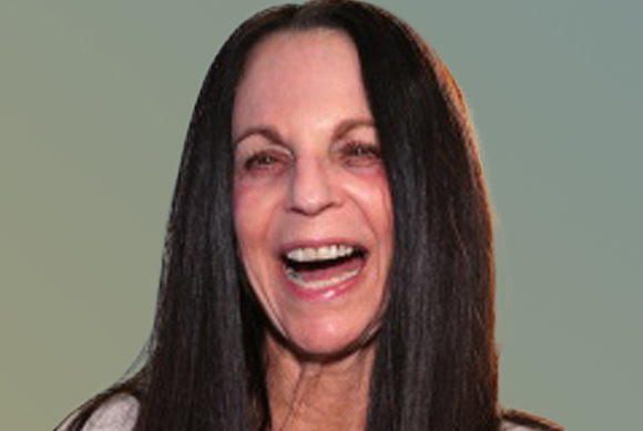 A woman with long dark hair smiles broadly with her mouth open against a solid green background.
