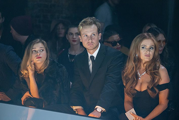 A group of people sitting in a dark venue, looking forward with serious expressions.
