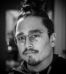 Black and white close-up portrait of a man with glasses and hair tied in a bun.