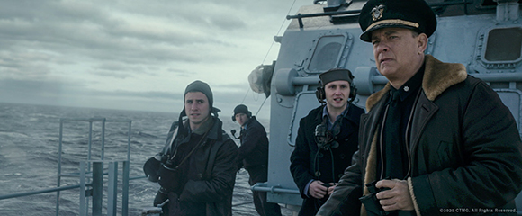 Four men in heavy coats and hats stand on the deck of a ship under a cloudy sky.