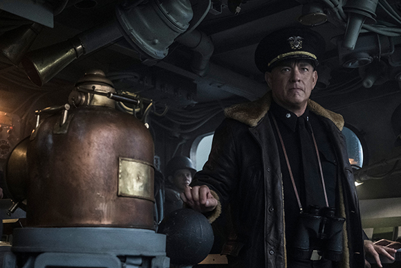 A man in a dark military uniform and fur-collared coat stands on a ship near a large copper vessel.