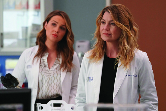 Two women wearing white medical lab coats stand in a clinical environment.
