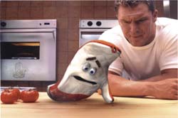 A man in a white t-shirt looks down at a piece of bread with a cartoon face on a kitchen counter.