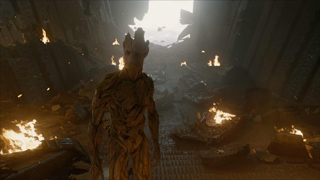 A tall, bark-textured humanoid figure stands in a dark, debris-filled corridor with fires burning in the background.
