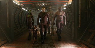 Five diverse characters walk toward the camera through a dimly lit, metallic spaceship hallway.