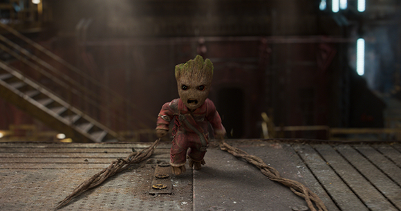 A small, tree-like creature with large eyes walks forward on a metallic floor with vines trailing behind.
