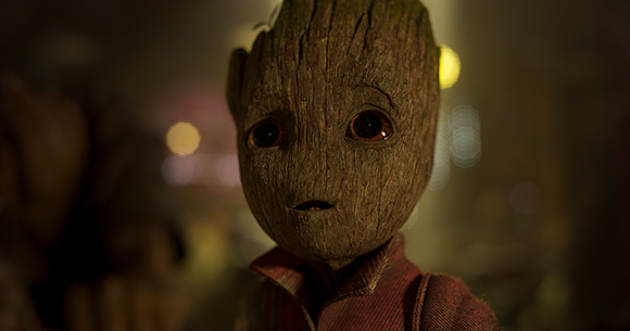 A small, sentient tree creature with large dark eyes and wood-textured skin wearing a red shirt.