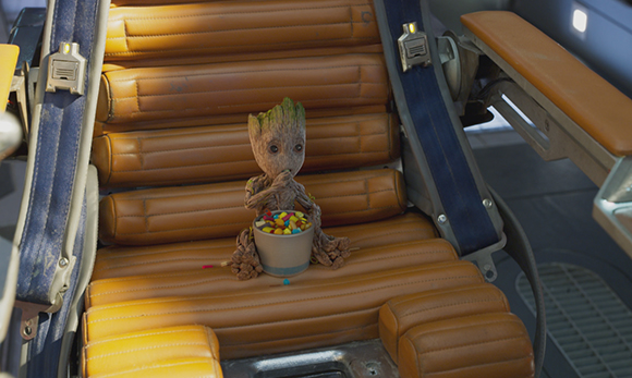 A small tree-like creature sits on a tan leather seat holding a bowl of colorful candies.