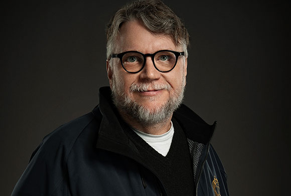 A man with short graying hair, glasses, and a salt-and-pepper beard smiling against a dark background.