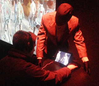 A person with headphones looks at a tablet displaying a historical scene, with a mannequin in a suit nearby.