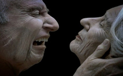 Profile view of an elderly man shouting and an elderly woman with her eyes closed being held by the chin.