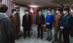 Six young men stand in a circle in a dimly lit room.